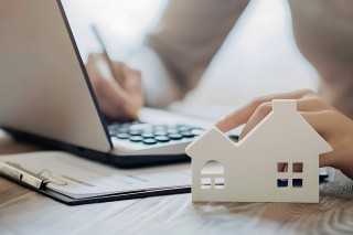 Foto: Person am Laptop mit Häuschen davor